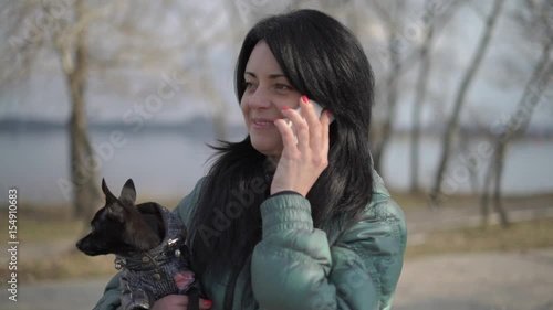 a Woman With a Dog Talking on Phone Sitting on a Park Bench Near the River photo