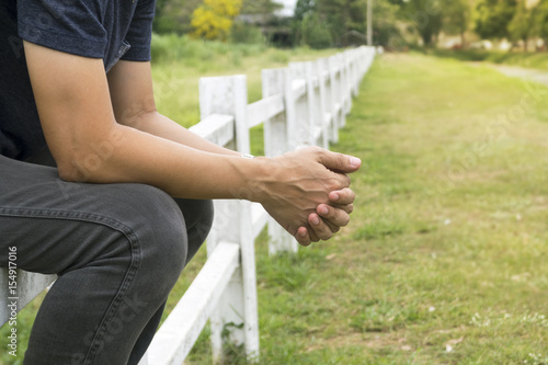 Man sitting on long white fence and crossed his fingers.