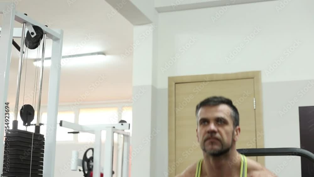 Fair-haired bearded man in a grey athletic shirt islifting dumbbells using simulator. Front shooting Fair-haired bearded man in a grey athletic shirt islifting dumbbells using simulator. Front shooting