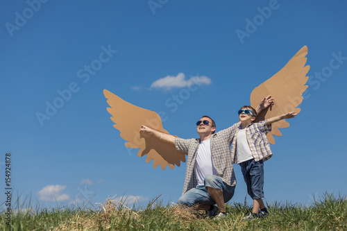 Father and son playing with cardboard toy wings in the park at the day time.