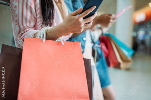 Close-up partial view of woman with shopping bags using smartphone, boutique shopping concept