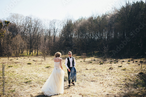 Bride in light dress walks to groom on the lawn in forest