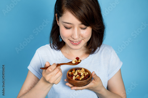 фотографія young woman eating granola on blue background