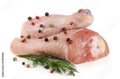 Two raw chicken drumsticks with a sprig of dill and peppercorns isolated on white background