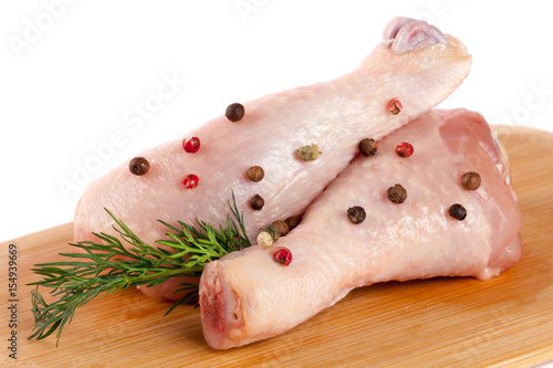 two raw chicken drumsticks on a wooden cutting boardn with a sprig of dill and peppercorns white background