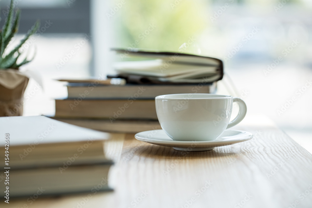 Close-up view of cup of coffee and notebooks on wooden table top