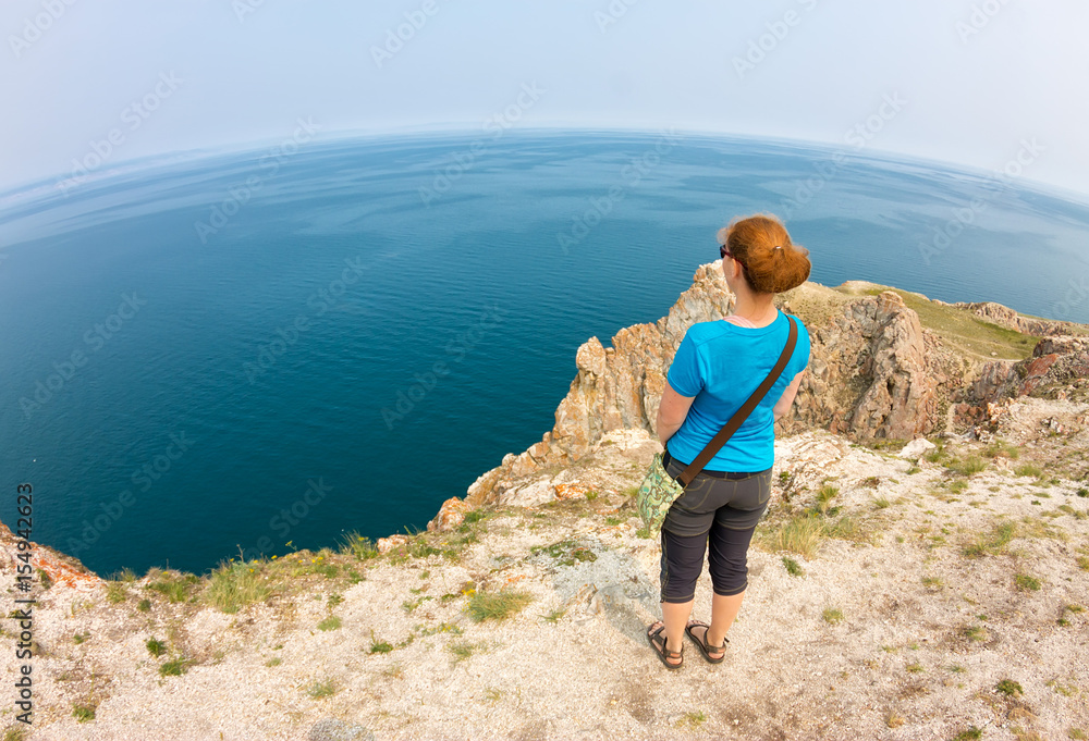 Red-haired girl stands on the edge of a cliff by the sea