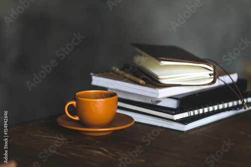 Close-up view of cup of coffee and notebooks on wooden table top