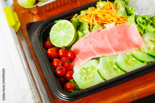 Delicious mediterranean-Style fresh salad with ham in a plastic box on wooden table photo