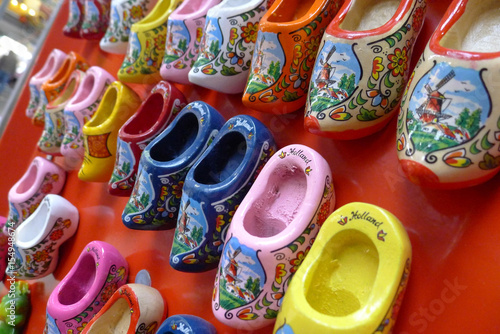 A collection of clogs in various colours with lovely decorations hanging on a wall.