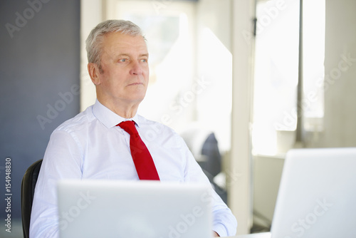 Contemplating his future. Shot of a senior financal advisor man looking thoughtfully while sitting at desk in the office and working on business presentation.  photo