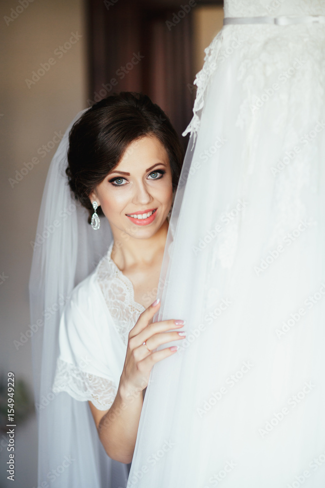 The charming bride stands near wedding dress The charming bride stands near wedding dress