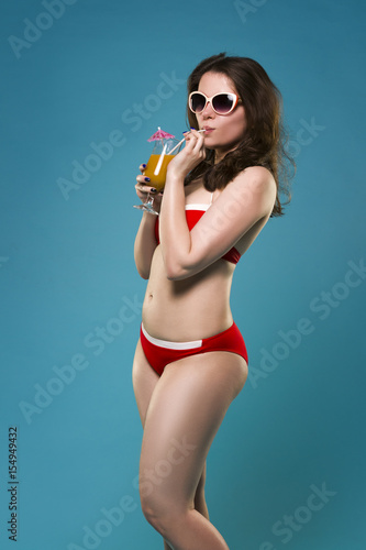 Beautiful young woman in red bikini with cocktail on blue background