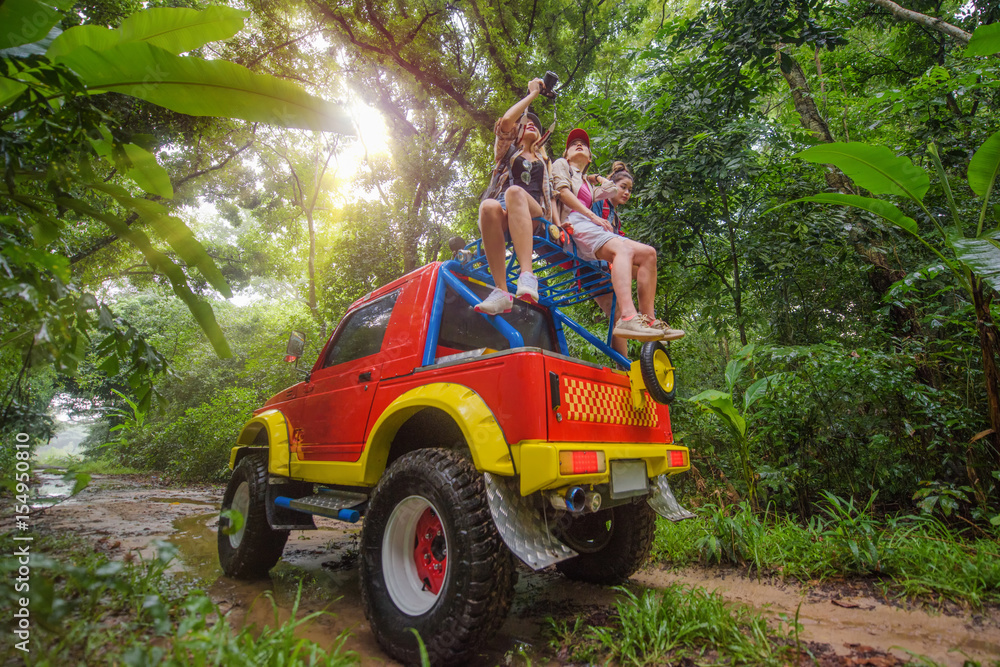 woman in group are enjoy traveling by sitting on the rack-roof of the convertible car off-road in jungle woman in group are enjoy traveling by sitting on the rack-roof of the convertible car off-road in jungle