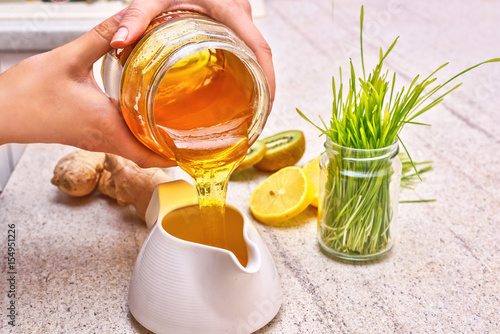 Golden liquid Organic Honey pouring from jar. Green wheat, lemon and ginger f...