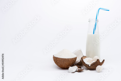 Close-up view of healthy coconut milk in glass bottle with straw and ripe coconut isolated on white