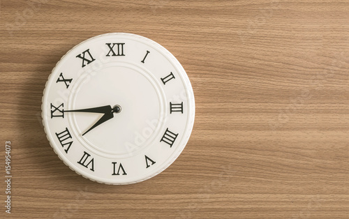 Closeup white clock for decorate show a quarter to eight o'clock or 7:45 a.m. on wood desk textured background with copy space