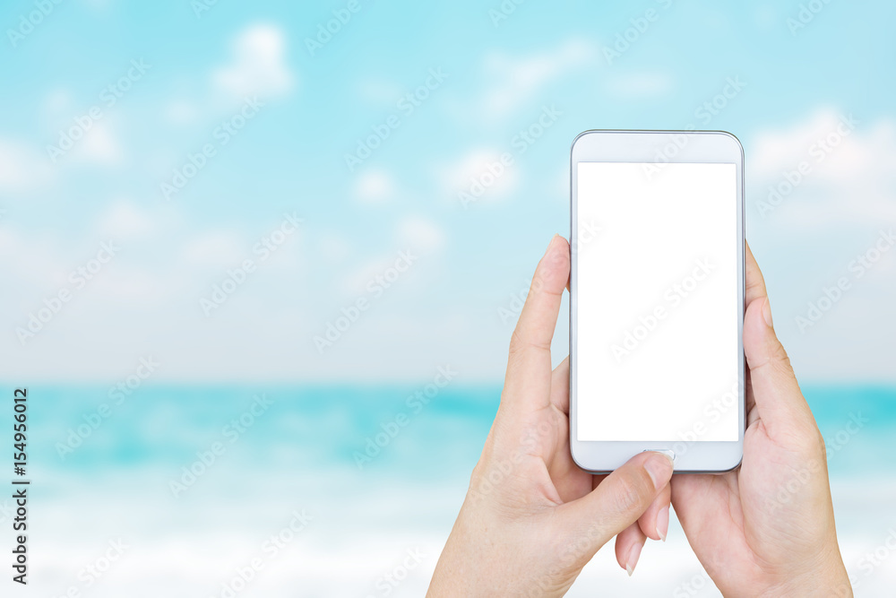 Woman's hand holding smart phone with blur beach and tropical sea.