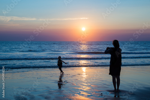Silhouettes of mother and child enjoying the sunset on the atlantic ocean, Lacanau France