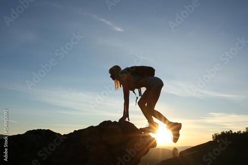 Woman tourist with backpack in tourist clothes climbs mountain. Silhouette against background sunrise