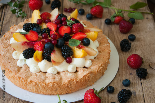 Homemade dacquoise cake with wipped cream cheese garnished with summer berries and peaches, close up.