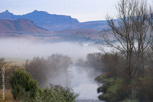 A river runs through the foothills of the Drakensberg Mountain Range at Underberg in South Africa.  This landscape-orientation takes in the mountains and a section of the Ngangwane River in the mist. © Fred