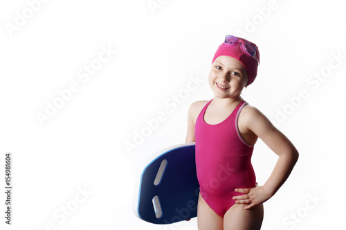 Swimmer: little (6 years old) caucasian girl in pink swimming costume, swimming cap and goggles holding a blue swimming board. Isolated on white background, empty space for text.