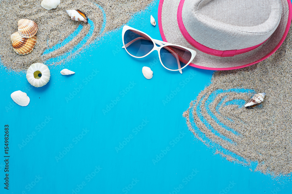 Naklejka premium Summer set. Beach vacation accessories sunglasses and hat flat lay on sand with seashells. Isolated on blue background.