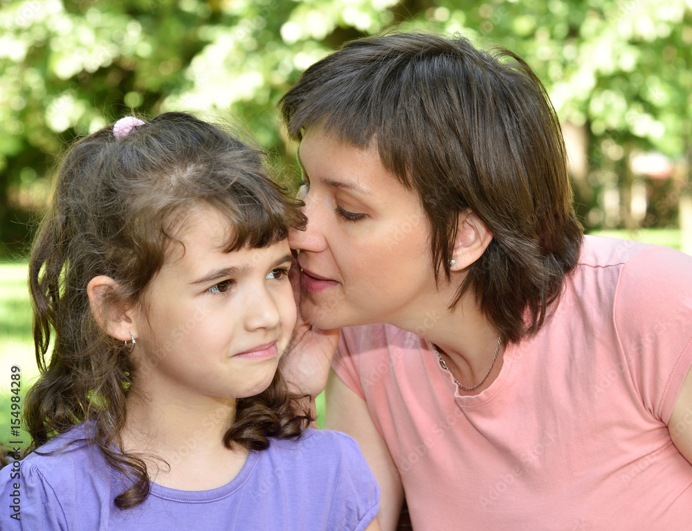 Mother whispering secret into ears of surprised daughter Mother whispering secret into ears of surprised daughter