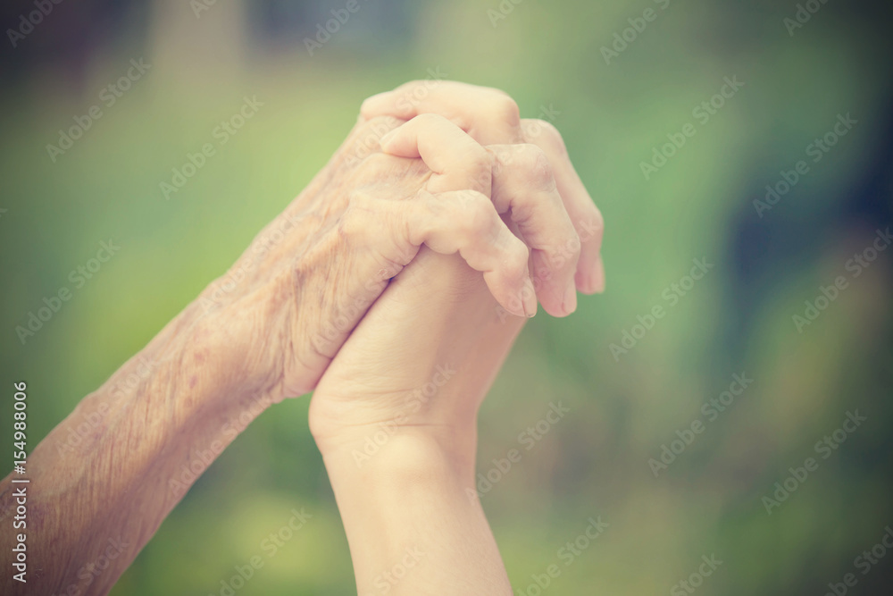 Old and young holding hands on light background, vintage tone. Old and young holding hands on light background, vintage tone.