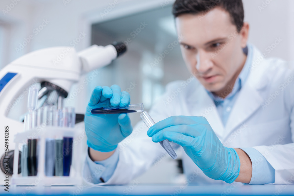 Fototapeta premium Attentive lab assistant pouring down blue liquid