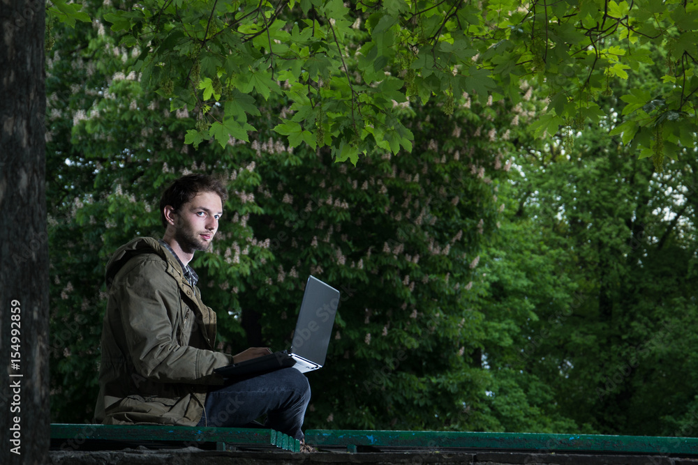 Young handsome student sitting on a wooden bench in the park with laptop computer. Young handsome student sitting on a wooden bench in the park with laptop computer.
