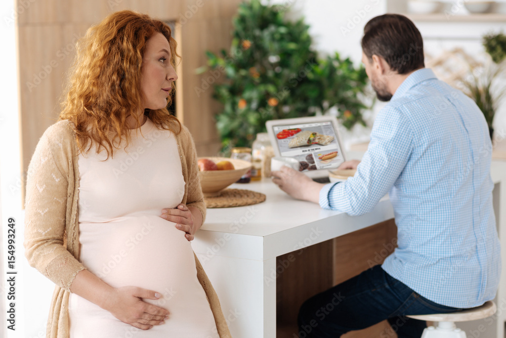 Pregnant woman sitting in kitchen and looking at husband Pregnant woman sitting in kitchen and looking at husband