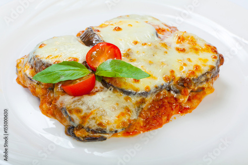Photos Baked eggplant with cheese, tomatoes and spices on a white plate