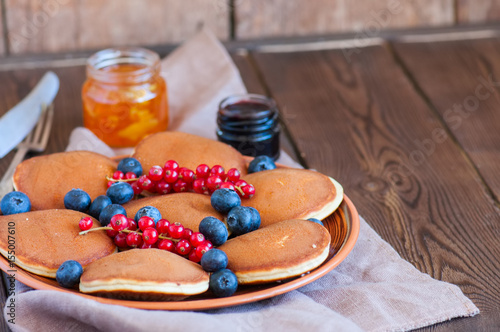 Stack of fluffy panckes with fresh berries, blueberry and orange jam served on a white plate. Healthy breakfast concept. photo