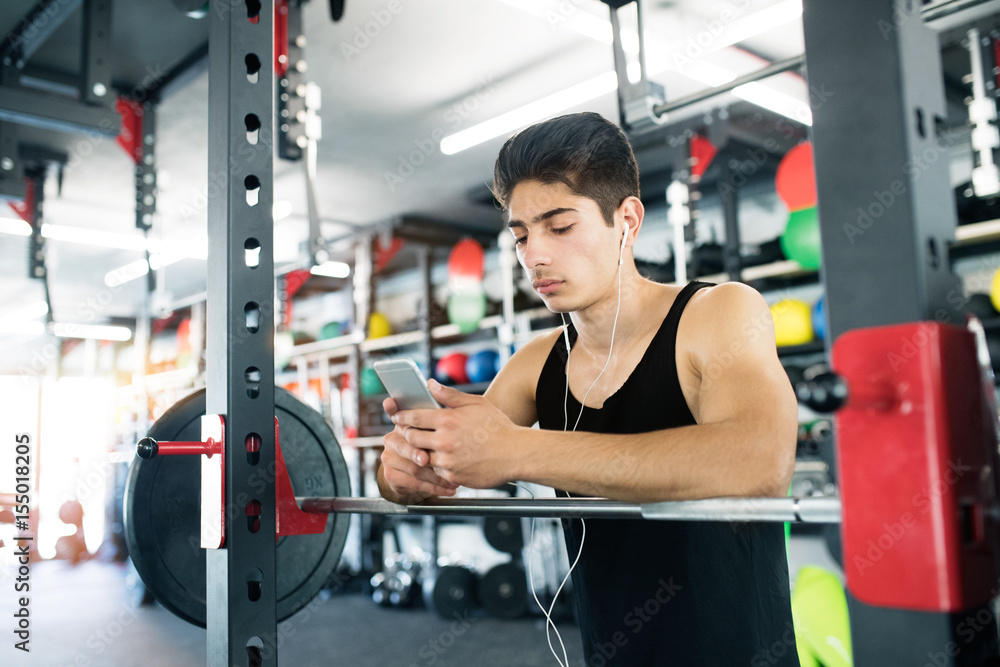 Hispanic man in gym resting, holding smart phone,listening music Hispanic man in gym resting, holding smart phone,listening music