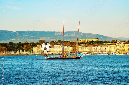 View of historic center of Geneva with a big football ball and yacht with people on Geneva Lake. Switzerland.