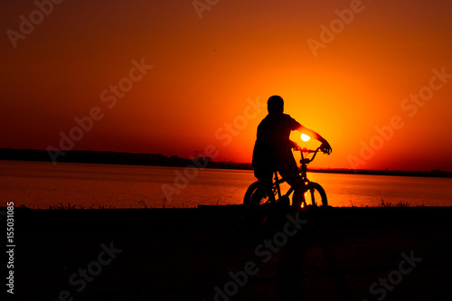 Silhouette of man biker cycling by the lake at sunset © Marius Comanescu