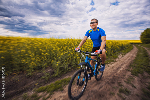 Fototapeta Naklejka Na Ścianę i Meble -  A male cyclist is riding on a picturesque yellow rapeseed field.