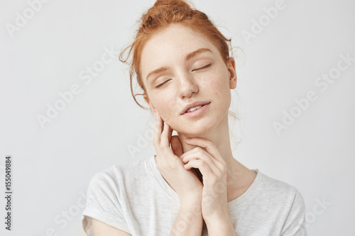 Portrait of tender girl with foxy hair and closed eyes smiling.