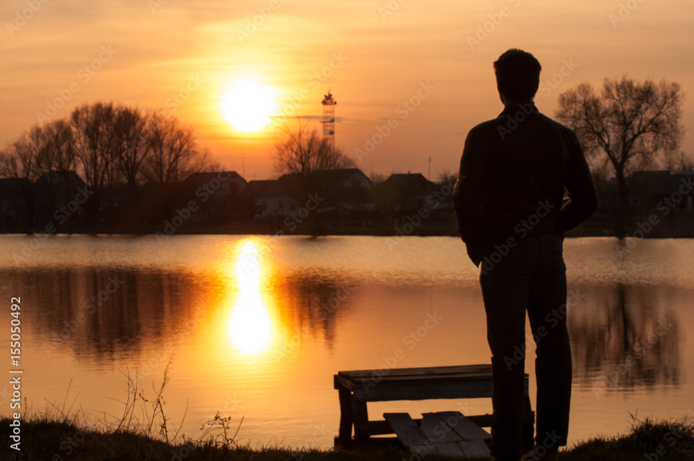 Fototapeta premium Man silhouette, standing on river stones gangway and contemplating a beautiful sunset.