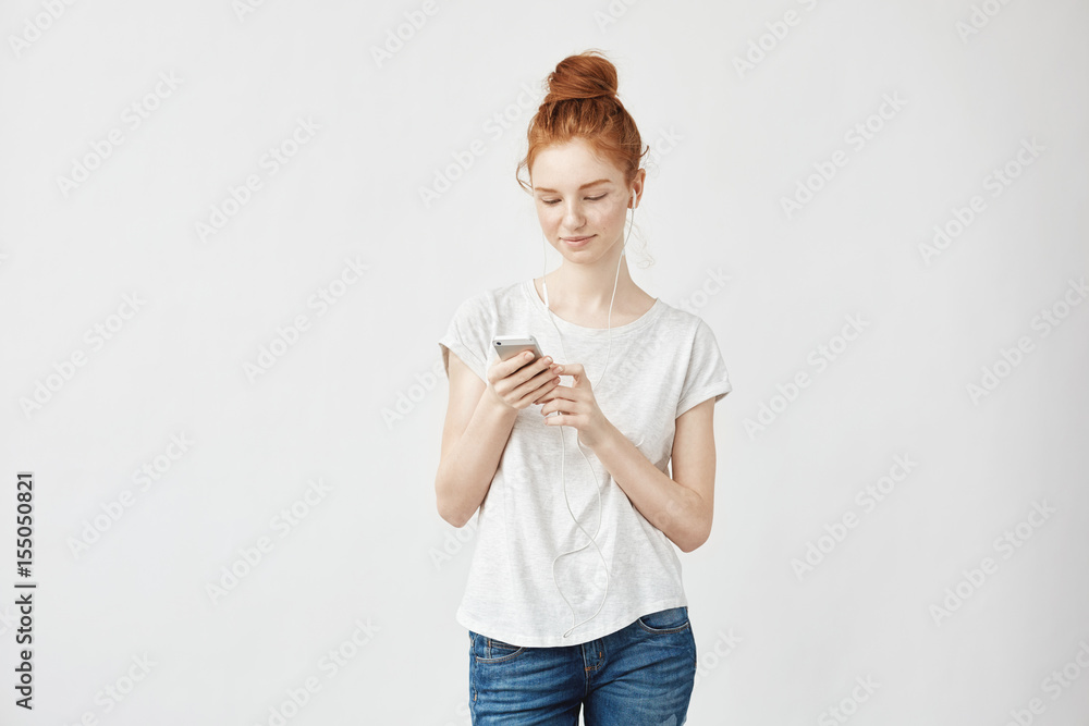 Ginger girl with freckles in headphones smiling looking at phone. Ginger girl with freckles in headphones smiling looking at phone.