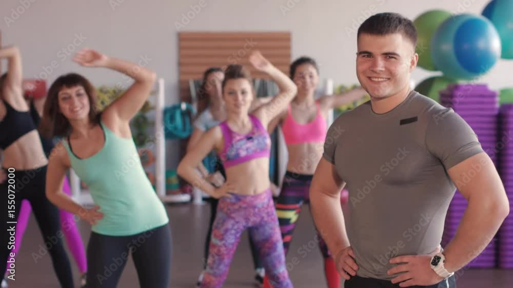 Close-up of male fitness trainer. He looks at a group of girls who train in an aerobic gym Close-up of male fitness trainer. He looks at a group of girls who train in an aerobic gym
