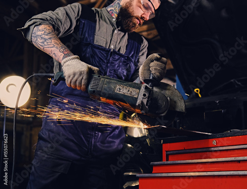 Mechanic cuts steel car part with an angle grinder.