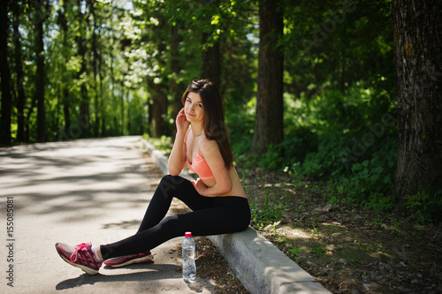 Fitness sport girl in sportswear sitting at road in park with water at bottle, outdoor sports, urban style.
