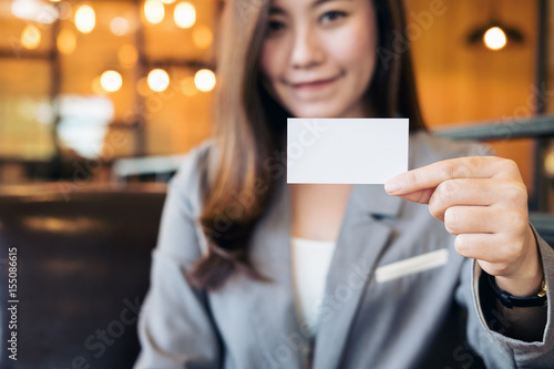 A beautiful Asian business woman holding and showing empty business card in modern loft cafe