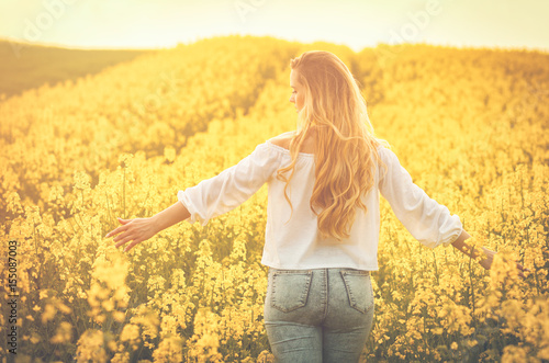 Woman with long hair back view in yellow rapeseed field at sunset