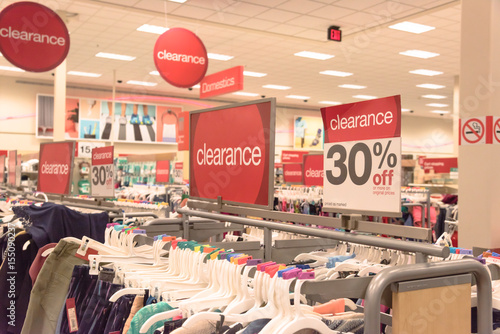 Red clearance sign for 30% off on cloth rack with variety of women apparel in retail store in America.