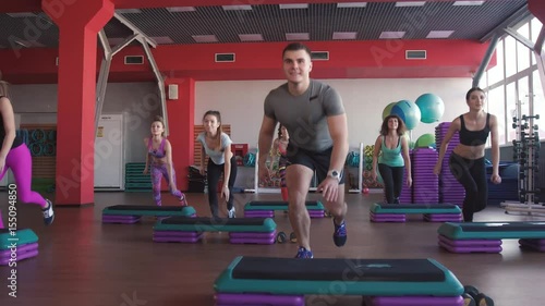 Step aerobics exercise class - group of people exercising on steppers with the trainer.