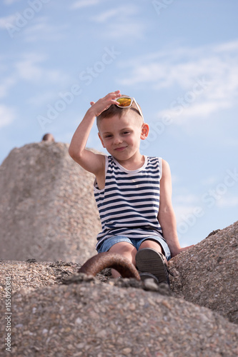 little boy with sunglasses and shirt sitting on the sea wall smiling